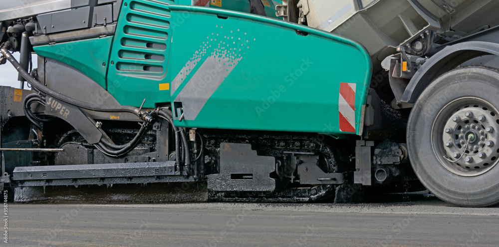 Fototapeta premium Asphaltfertiger wird von LKW mit Asphalt beladen