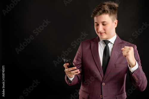 Law student with blond hair dressed in burgundy jacket, white shirt and black tie reading and sending text messages on cellphones happy face