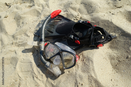 Diving equipment left on sandy beach on sunny day, close up. Fins and snorkeling mask laying in sand. Summertime