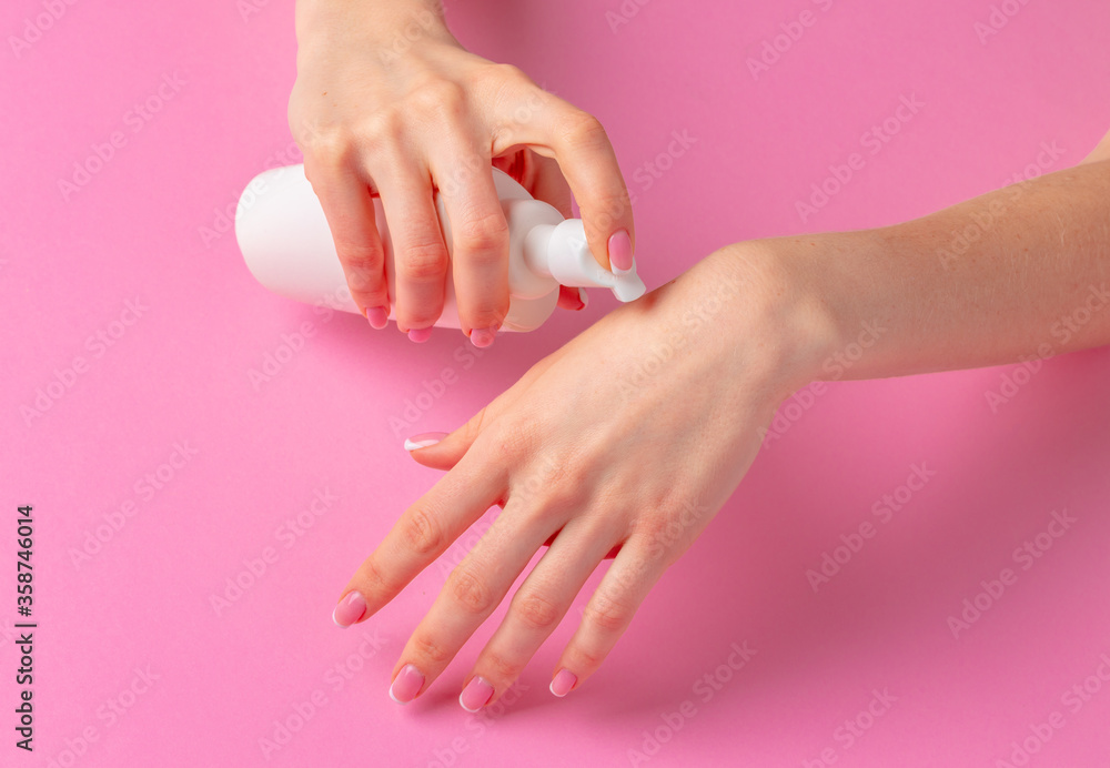 Female hand holding skincare product bottle on pink Female hand holding skincare product bottle on pink
