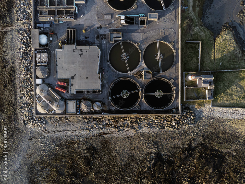 Aerial drone top down view on a biological sewage water treatment plant. Round tanks and factory shops. Security fence perimiter.