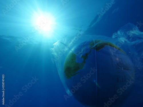 world in plastic bag drifting underwater representing ocean pollution with sun beams and rays 