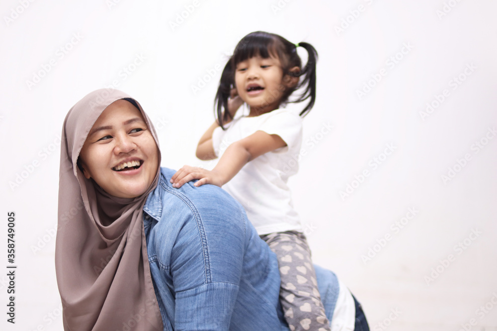Asian muslim mother playing with her little baby girl daughter sit on her back, acting like a horse for her kid, happy smiling Asian muslim mother playing with her little baby girl daughter sit on her back, acting like a horse for her kid, happy smiling