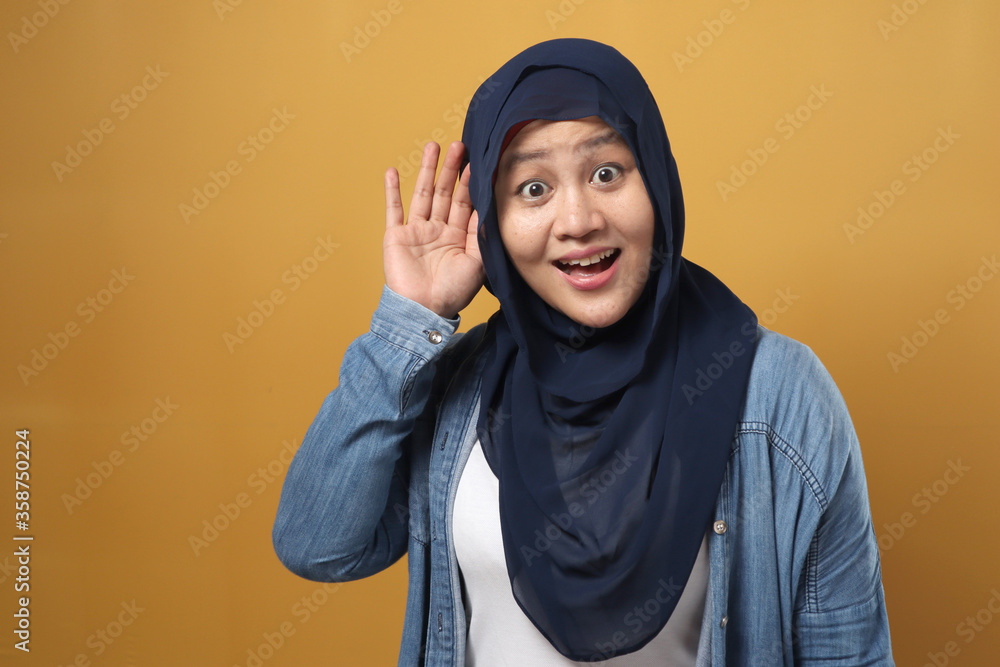 Asian muslim woman wearing hijab smiling while doing hearing gesture, shocked surprised expression to hear gossip Asian muslim woman wearing hijab smiling while doing hearing gesture, shocked surprised expression to hear gossip