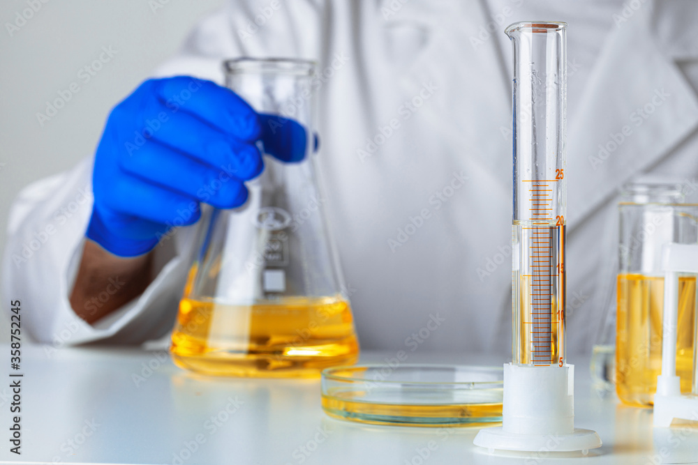 Scientist or doctor in blue gloves pouring some yellow liquid into a flask Scientist or doctor in blue gloves pouring some yellow liquid into a flask