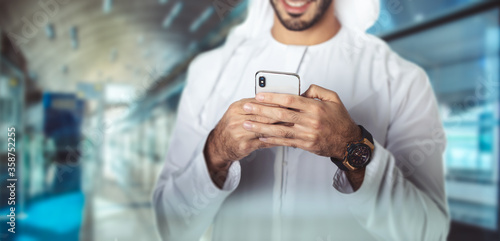 Close up shot of Arab Middle East man using smart mobile phone device browsing the internet or reading emails wearing Kandura and Ghutra