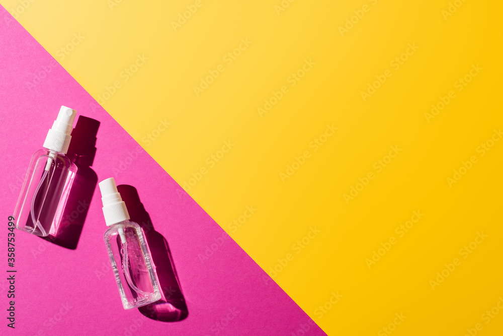 top view of transparent spray bottles with disinfectant on pink and yellow top view of transparent spray bottles with disinfectant on pink and yellow
