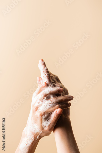 partial view of woman washing hands with soap foam isolated on beige