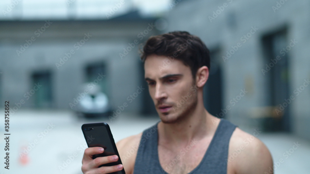 Closeup athlete man looking smartphone on street. Smiling man reading message Closeup athlete man looking smartphone on street. Smiling man reading message