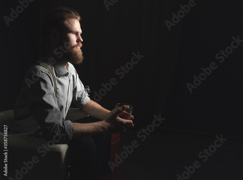 Portrait of a pensive handsome young man, with a glass of alcohol in his hands, on an isolated black background. The concept of pastime, rest and relaxation