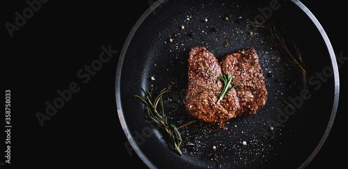 Grilled beef steak in frying pan, on black background with copy space