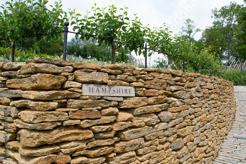A sign of the county of Hampshire set into dry stone wall within a garden.
