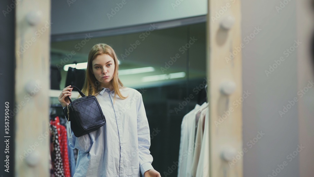 Attractive woman trying on handbags in front of a mirror in a boutique
