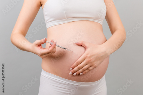 Close up of pregnant woman making injection of insulin in her belly at colorful background with copy space. Sugar control during pregnancy concept