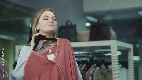 Foto Attractive female customer looking at the mirror and trying on blouse in fitting