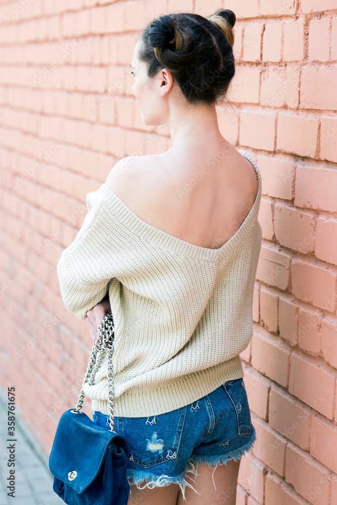 Girl in a beige sweater and jeans shorts posing on the street.
Girl in a beige sweater and jeans shorts posing on the street.