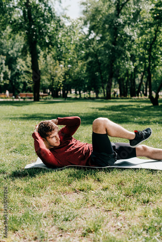 Side view of sportsman doing abs while working out on fitness mat in park