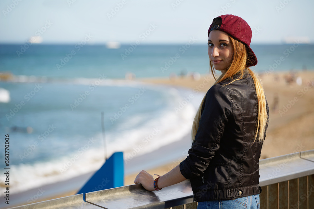 Half length portrait of stylish hipster girl standing on the pier of beautiful beach, young woman enjoying beautiful afternoon outdoors with blue sea on background, promenade at sunny day
