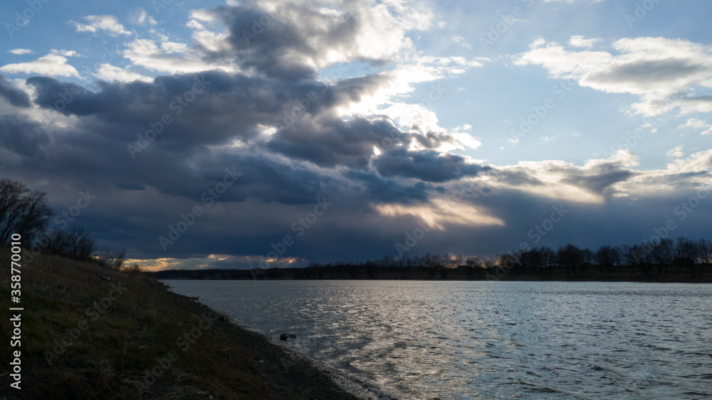 The sun’s rays break through the gloomy storm clouds above the river.