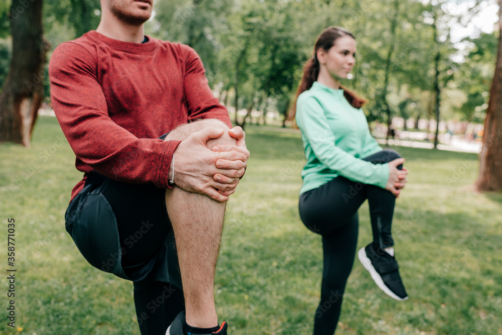 Selective focus of couple stretching legs while working out in park