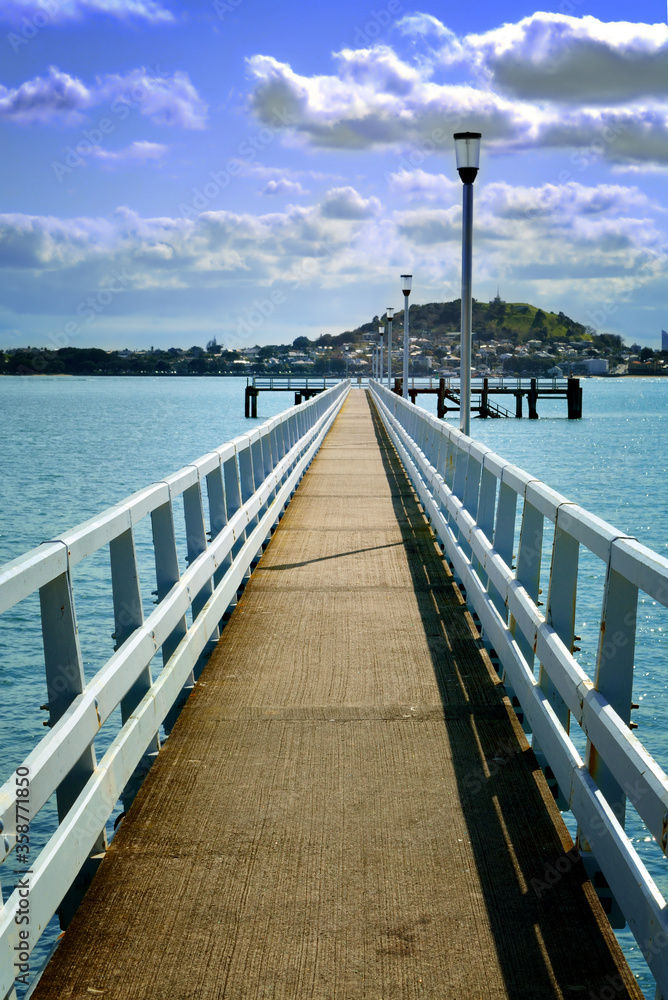 Pier with lamp posts over blue water under cloudy sky