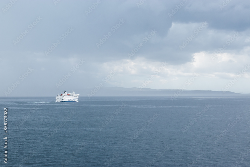 Fototapeta premium Big white Croatian ferry sailing out of Split going to the islands. Alone on the sea on a rainy storm day, dark clouds stretching into the distance
