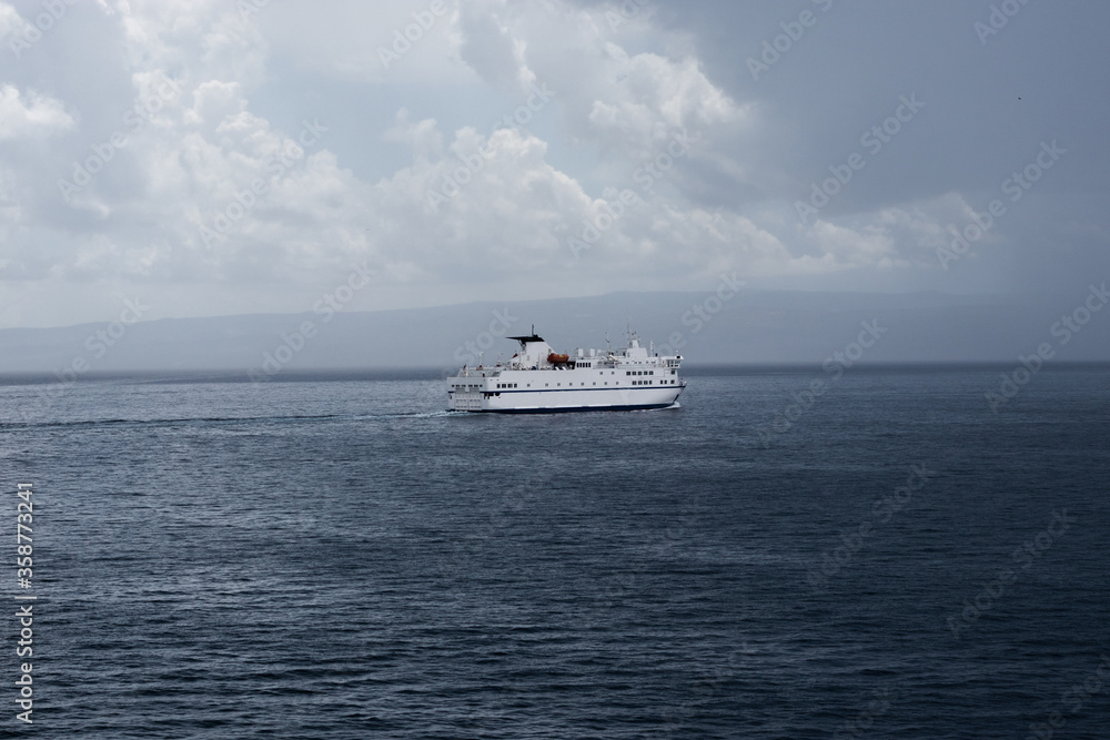Big white Croatian ferry sailing out of Split going to the islands. Alone on the sea on a rainy storm day, dark clouds stretching into the distance