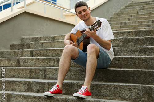 Young man sits on the steps and play on guitar