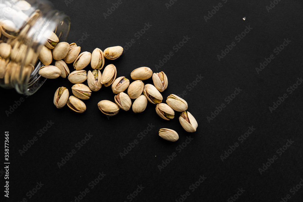 Pistachio scattered on the black table from a jar. Walnut is a healthy vegetarian protein nutritious food. Pistachio scattered on the black table from a jar. Walnut is a healthy vegetarian protein nutritious food.