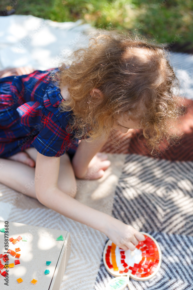 Little girl creates a ceramic mosaic on a plaid in the garden. Little girl creates a ceramic mosaic on a plaid in the garden.