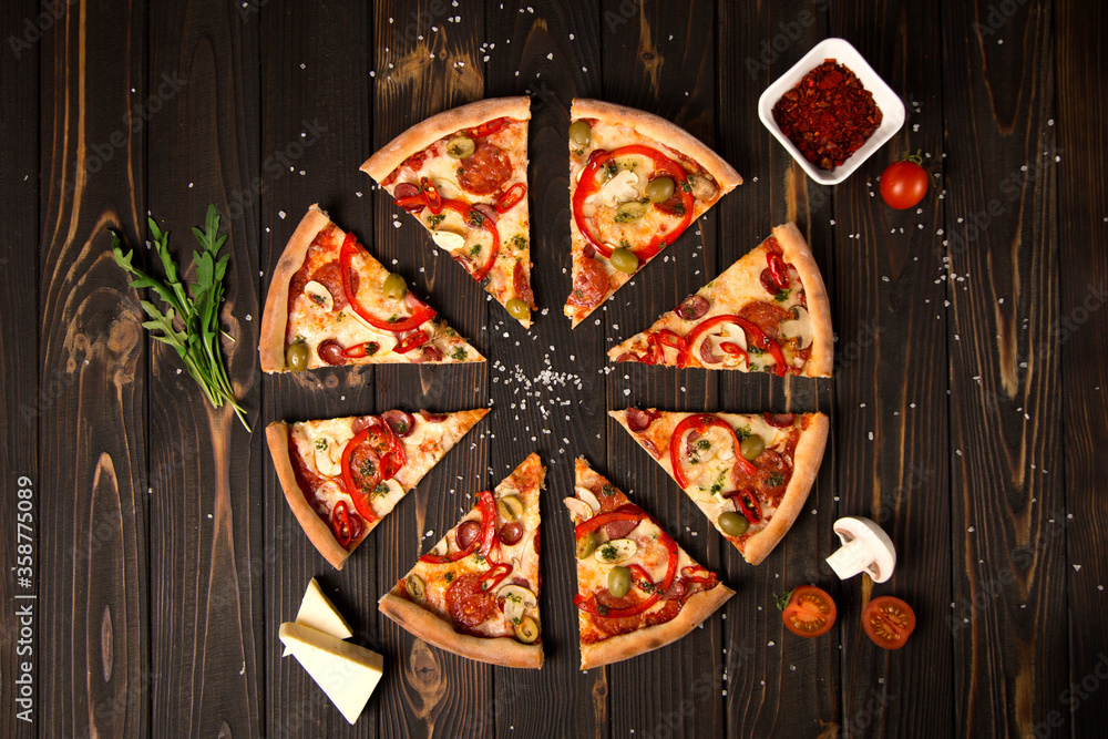 Top view of sliced pizza with bell pepper, green olives, sausages, mozzarella cheese, pepperoni, salami, chili pepper, champignons on wooden background. Tasty pizza pieces. Fast food delicious dish
