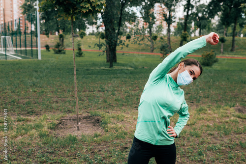 Sportswoman in medical mask exercising in park