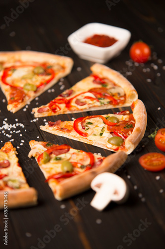 Top view of sliced pizza with bell pepper, green olives, sausages, mozzarella cheese, pepperoni, salami, chili pepper, champignons on wooden background. Tasty pizza pieces. Fast food delicious dish 