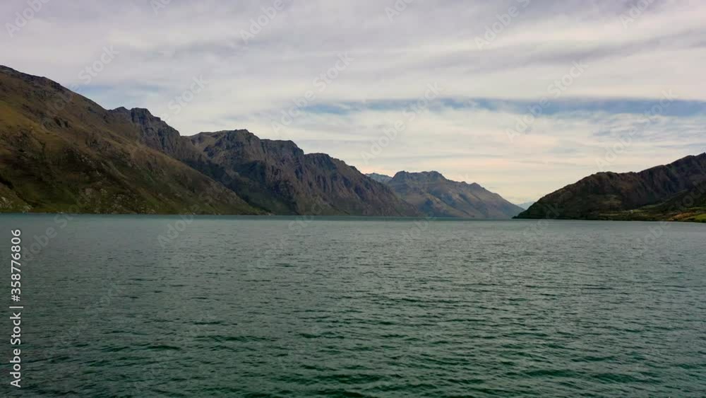 Aerial shot of rippled lake amidst mountain range against sky, drone flying forward over water - Queenstown, New Zealand Aerial shot of rippled lake amidst mountain range against sky, drone flying forward over water - Queenstown, New Zealand