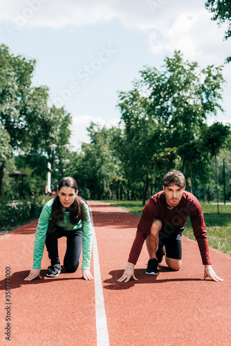 Young couple in starting position on running track in park