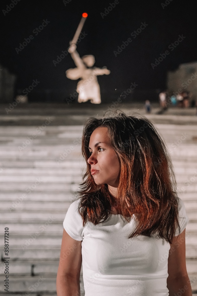 Portrait of a brunette girl with long hair at night against the background of Mamayev Kurgan and sculpture Portrait of a brunette girl with long hair at night against the background of Mamayev Kurgan and sculpture