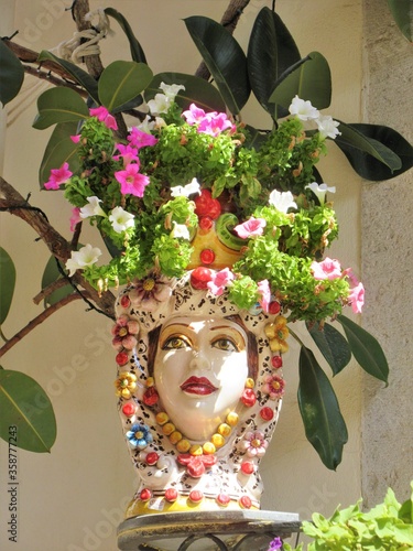 Fototapeta Naklejka Na Ścianę i Meble -  Italy, Sicily, Taormina / 2018 August 21st / Traditional decorative ceramic vase on a balcony in Taormina, woman face with white and pink flowers