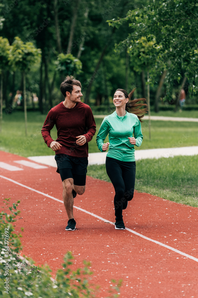 Selective focus of sportswoman smiling at boyfriend while jogging in park