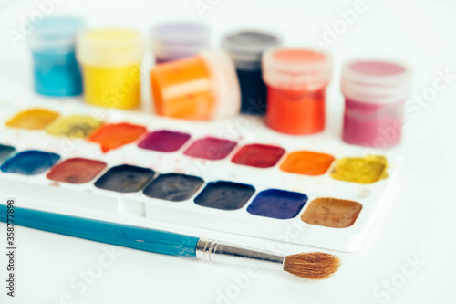 Colorful gouache paints and brush for painting on white wooden table. Copy, empty space for text