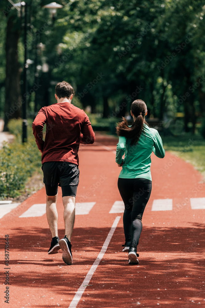 Back view of couple running on running path in park
