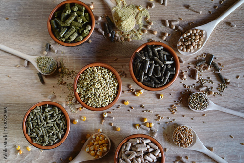 Different kinds of pelleted compound feed in bowls and spoons on wood table, copy space. Top view, flat lay