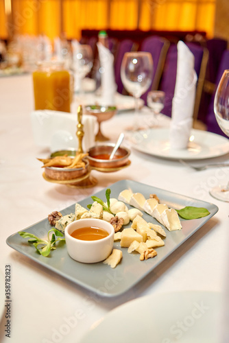 Cheese plate with honey and nuts on holiday dinner table, copy space. Wedding or birthday reception