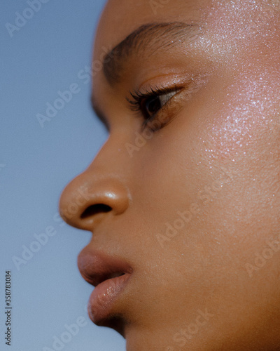Close up portrait of dark-skinned young model on background of blue sky with natural make-up