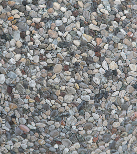 Multi-colored sea pebbles at pathway outdoors. Small round stones are in cement mortar. Selective focus at centre of image. Abstract texture or background.