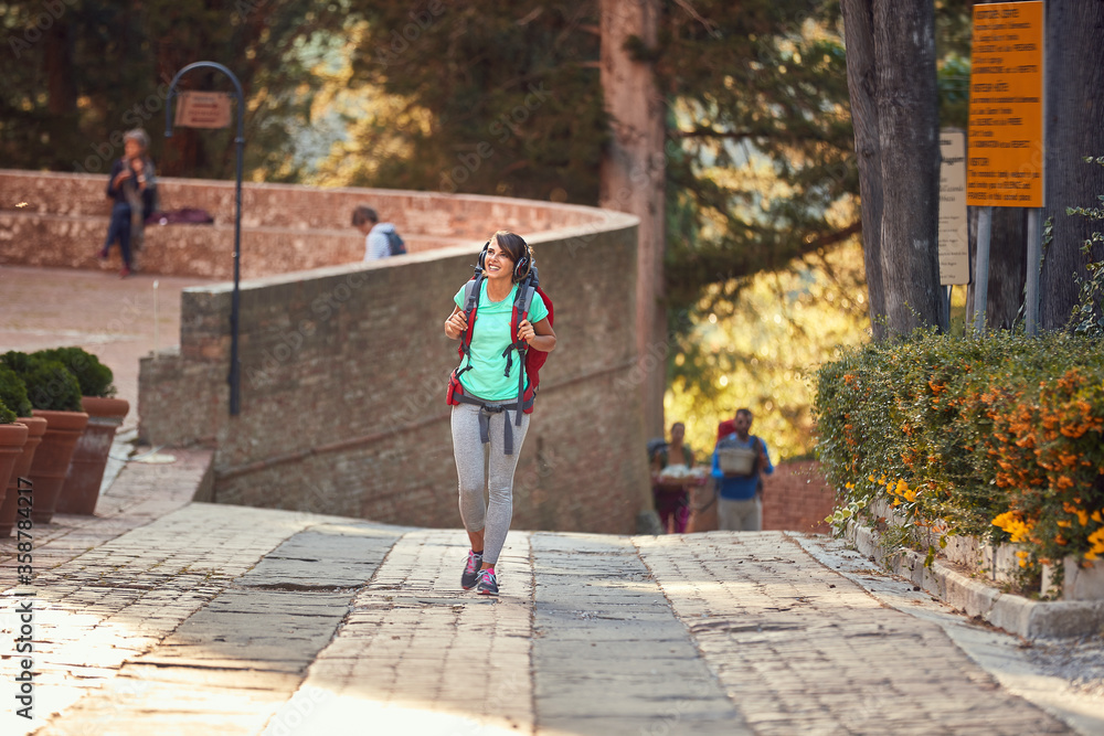 female enjoying in active sightseeing in italy, walking with backpack, head up, smiling