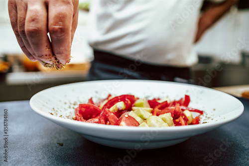 Chef in the restaurant preparing salad from fresh tomatos and cucumbers