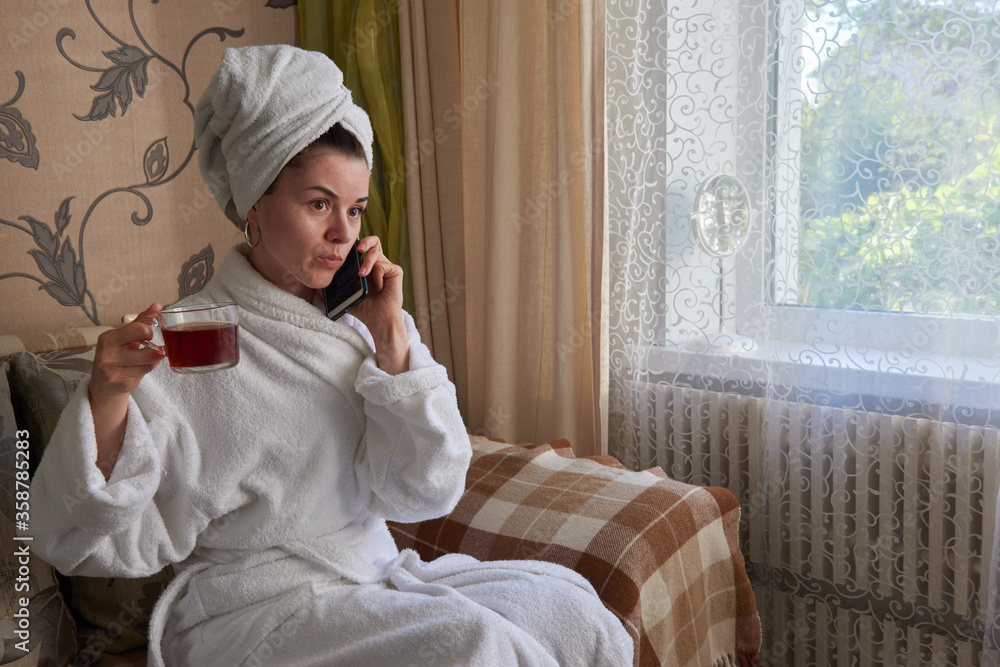 girl sitting on a sofa in a white bathrobe with a phone in her hand in a spa girl sitting on a sofa in a white bathrobe with a phone in her hand in a spa