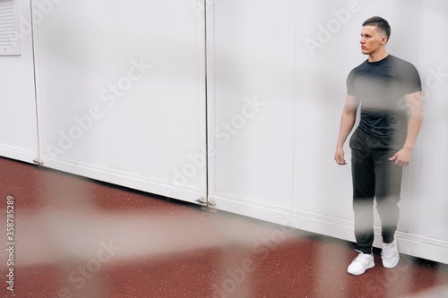 A pensive Caucasian fitness trainer in full growth stands on light background. Conceptual photo on the sports ground  online training