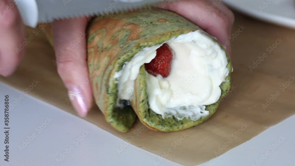 Woman slices cooked Swiss roll. Mint and spinach roll with cream and strawberry filling. Woman slices cooked Swiss roll. Mint and spinach roll with cream and strawberry filling.