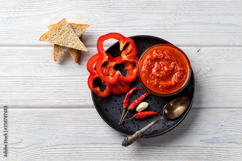 Ajvar or pindjur red vegetable sauce, paprika pepper on a black plate and wooden table. Serbian traditional food photo